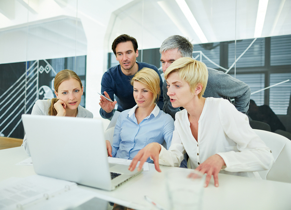 Group of colleagues looking at a laptop screen together.
